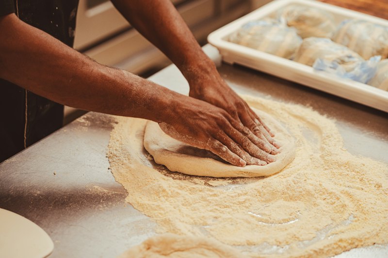 Deux mains étalent une pâte à pizza sur un plan de travail fariné.